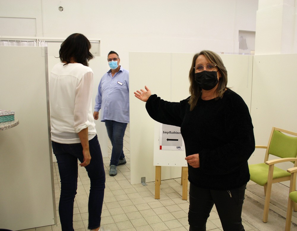 Eine Frau mit Mundschutz weist einer anderen den Weg, im Hintergrund wartet ein Mann im hellblauen Hemd. (Bild: LWL/SchuFi)