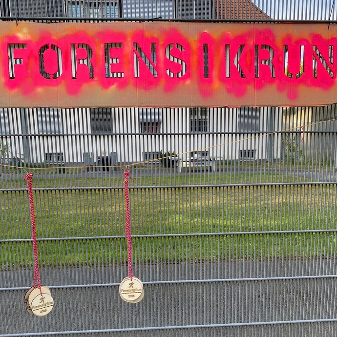 Medaillen aus Holz hängen an einem Gitterzaun unter einem Schild "Forensik-Run" (Bild: LWL/Schufi) (vergrößerte Bildansicht wird geöffnet)