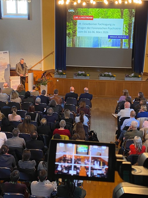 Ein Redner vor Publikum, auch zu sehen auf dem Display einer Filmkamera (Foto: LWL/SchuFi) (vergrößerte Bildansicht wird geöffnet)