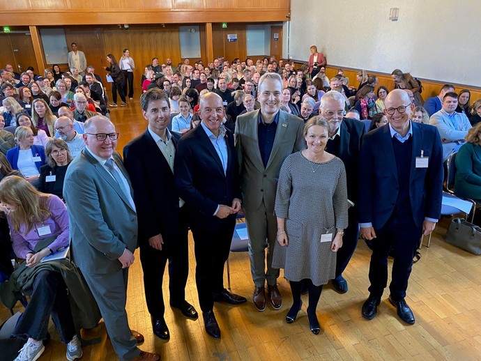 Eine Gruppe von Männern und Frauen steht mit dem Rücken zu einem voll besetzen Publikumsraum und lächelt in die Kamera (Bild: LWL/Schufi)
