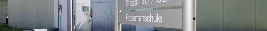 Blick auf ein Gebäude mit einer hohen Mauer und einem großen Tor, davor ein Schild, auf dem unter anderem Patientenschule steht. (Bild: LWL/Arendt).